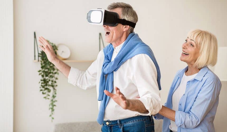New feelings. Excited mature man using the VR glasses, wife standing behind husband